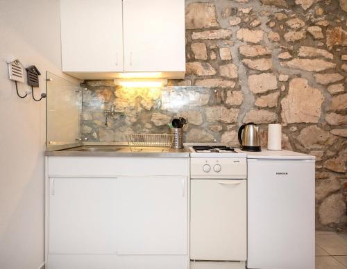 - une cuisine avec des placards blancs et un mur en pierre dans l'établissement Apartments Lotti, à Stari Grad