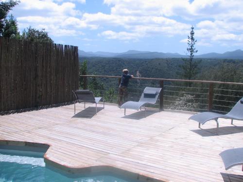 a man standing on a deck with chairs and a pool at Forest Valley Cottages in Knysna