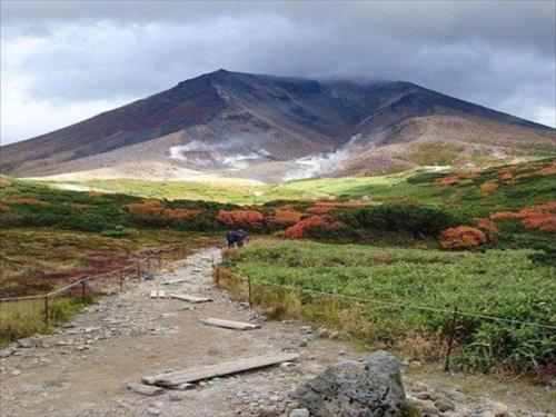 a mountain in the distance with a dirt road at K's House Hokkaido - Asahidake Onsen Hostel in Higashikawa