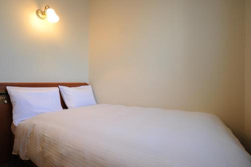 a bedroom with a bed with white sheets and a light at Suizenji Comfort Hotel in Kumamoto