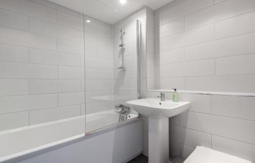 La salle de bains blanche est pourvue d'un lavabo et d'une baignoire. dans l'établissement The South Kensington Mews - Lovely 5BDR Home, à Londres