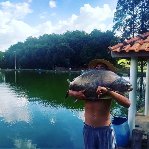 a man holding a fish in front of a lake at Pousada & Pesca Esportiva Fazolin in Socorro