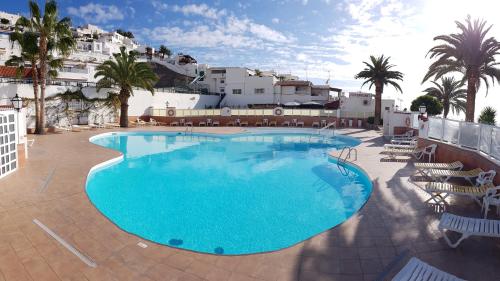 a large swimming pool with chairs and palm trees at Casa La Vista - Bungalow with fantastic sea views in Arguineguín