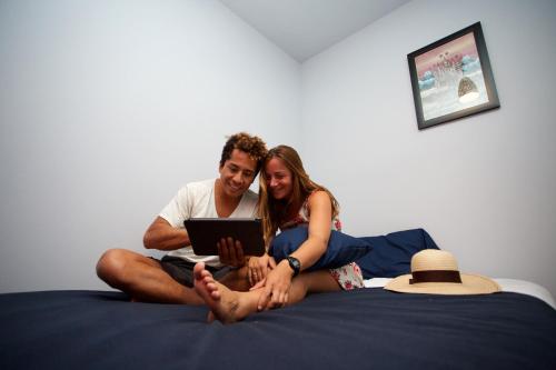 a man and woman sitting on a bed with a tablet at Hostel Auikyani in Cozumel
