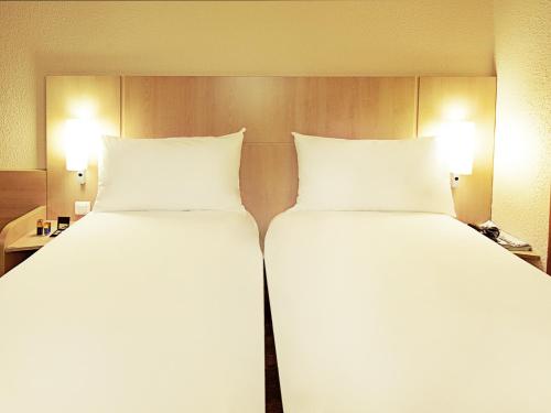two beds in a hotel room with white pillows at Hotel ibis Lisboa Jose Malhoa in Lisbon