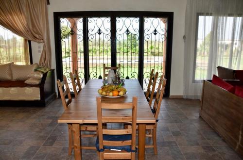 una mesa de madera con sillas y un bol de fruta. en Villa Moderne dans la Ferme "Belkheir" avec Piscine, Chevaux et Aire de Jeux pour Enfants, en Berrechid