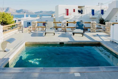 a swimming pool with chairs on a patio with the ocean in the background at Aeris suites in Koufonisia