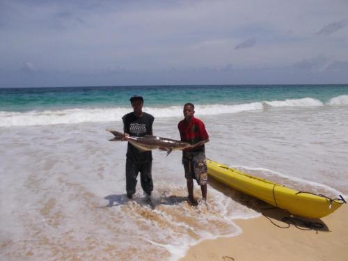 two men standing on the beach next to a boat at Treehouse Apartment at La Lodge at Long Bay in Corn Island
