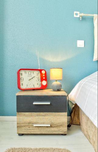 a red clock on a night stand next to a bed at Le Contemporain in Montbéliard