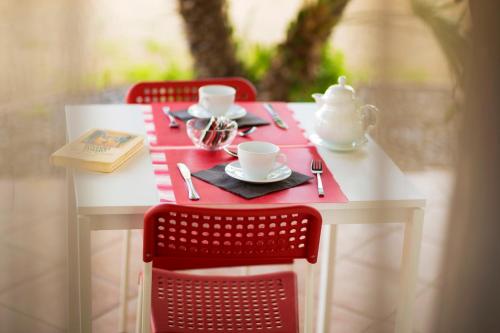 a table with two red chairs and a red and white table with cups and plates at Kòre rooms in Castellammare del Golfo