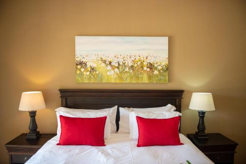 a bedroom with a bed with red pillows and a painting at Nkomazi Kruger Lodge & Spa in Malelane