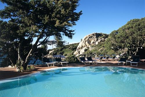 a large swimming pool with chairs and a mountain at Grand Hotel Smeraldo Beach in Baja Sardinia