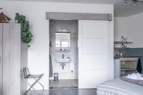 een slaapkamer met een deur naar een badkamer met een wastafel bij BnB 't Kraaiennest in De Cocksdorp