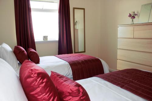 a bedroom with two beds with red pillows and a window at The Glebe, Am Fasgadh in Bowmore