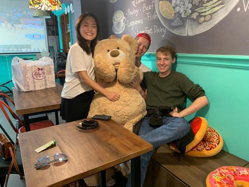three people posing with a large teddy bear at a table at mydeer backpacker in Tainan