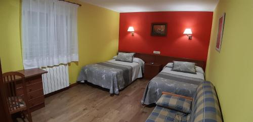 a room with two beds and a red wall at Pensión Toranda in Niembro