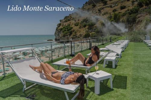 two people laying on lounge chairs at the beach at Holiday Lodge al Porto in Mattinata