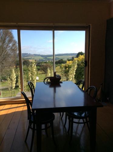 a dining room table and chairs in front of a large window at Cherry Top Farmstay - Boutique Eco Village in Lilydale
