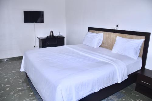 - une chambre avec un grand lit et des draps blancs dans l'établissement Hôtel La Couronne RW, à Yaoundé