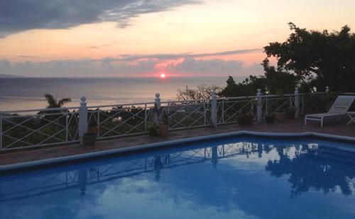 a swimming pool with a view of the ocean at sunset at Polkerris Bed & Breakfast in Montego Bay