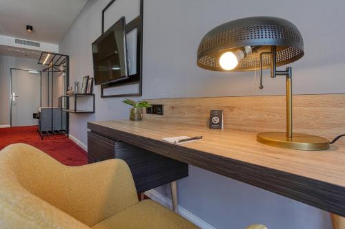 a desk with a lamp and a chair in a room at Centro Hotel Stern Ulm City, Trademark Collection by Wyndham in Ulm