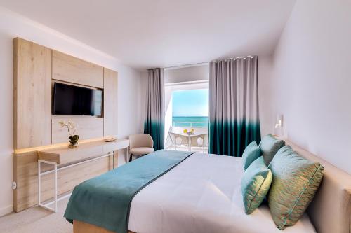 a hotel room with a bed and a desk and a window at Hotel Sol e Mar Albufeira - Adults Only in Albufeira