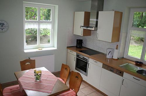 eine Küche mit einem Tisch und Stühlen sowie eine Küche mit weißen Schränken in der Unterkunft Ferienhof Wroge in Wietzendorf
