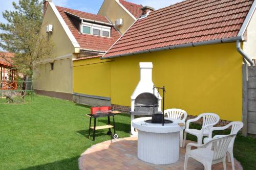 a backyard with chairs and a grill and a yellow house at Liliom Apartman in Gyula