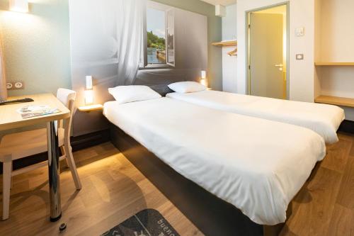 two beds in a room with a table and a desk at B&B HOTEL Laval Changé in Changé
