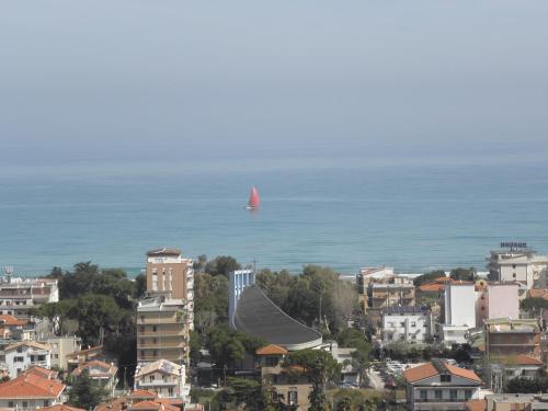 a red sailboat in the ocean with a city at Terrazza sul Mare in Giulianova