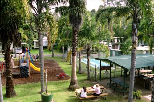 2 personnes assises sur des bancs dans un parc avec une aire de jeux dans l'établissement Batemans Bay Holiday Park & Hostel, à Batemans Bay