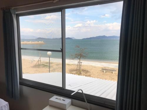 a window with a view of a beach and the ocean at Megijima Island Guesthouse & cafe Megino in Takamatsu