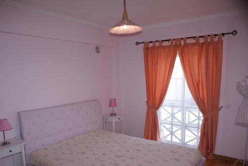 アルマンシルにあるApartamento Felicidadeのベッドルーム1室(オレンジ色のカーテンと窓付きのベッド1台付)