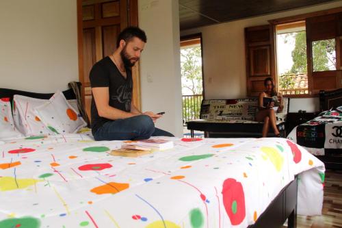 a man sitting on a bed looking at his cell phone at Eco Hotel El Columpio in Salento