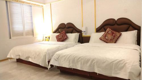 a bedroom with two beds with white sheets and red pillows at Aloha Hotel in Keelung