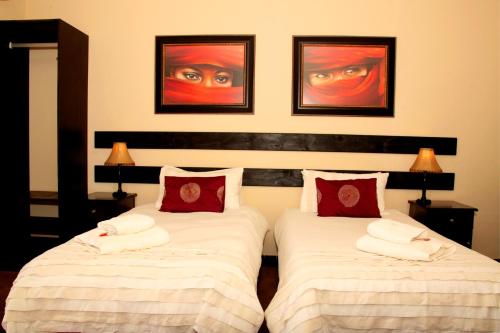 a bedroom with two beds with white sheets and red pillows at Hadassa Guest House in Otjiwarongo