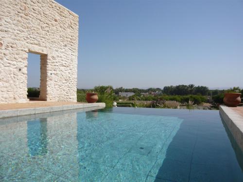 a large swimming pool next to a stone house at Villa Azir in Ghazoua