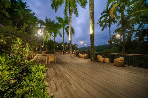 una terrazza in legno con sedie e palme di notte di The Payogan Villa Resort and Spa ad Ubud