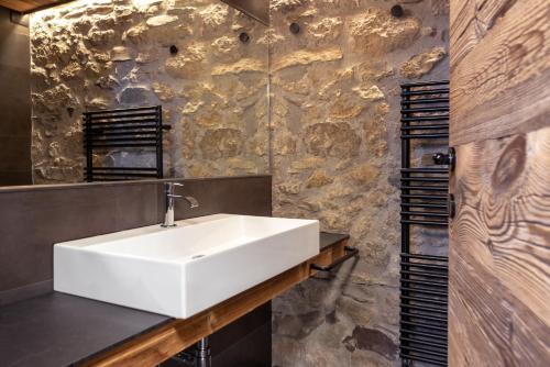 baño con lavabo blanco y pared de piedra en Pa' Sefn, en Sauris