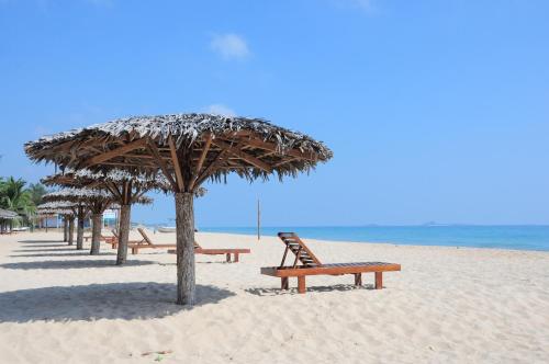 a row of benches on the beach with umbrellas at Mithra Paradise Beach Hotel in Nilaveli