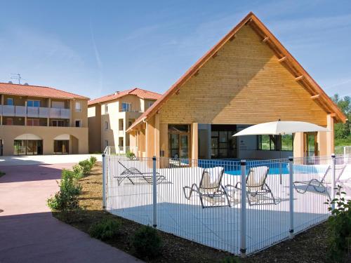 a fence with chairs and an umbrella next to a building at Lagrange Vacances Le Clos des Vignes in Bergerac