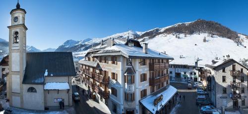 a building with a clock tower in front of a mountain at Hotel Compagnoni in Livigno