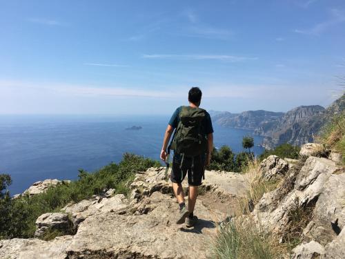 a man with a backpack walking on a mountain overlooking the ocean at Songbird in Agerola