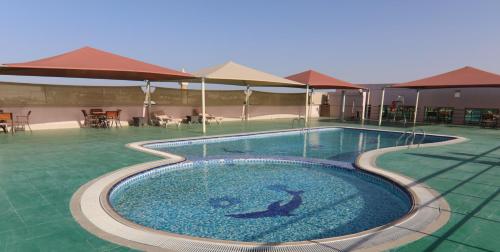 a large swimming pool in a resort with tables and umbrellas at All Seasons Hotel Al Ain - Previously City Seasons in Al Ain