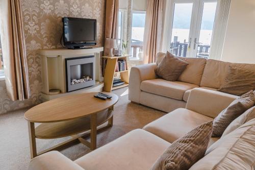 ein Wohnzimmer mit einem Sofa, einem Tisch und einem TV in der Unterkunft Bonnie Banks Lodge Ardlui in Ardlui