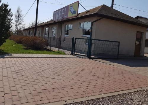 a building with a fence next to a brick sidewalk at Restauracja Zajazd Trefl in Czarlin