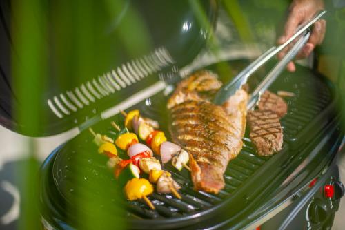 a person holding a grill with meat and vegetables at The Residence Maldives at Dhigurah in Gaafu Alifu Atoll