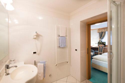 a white bathroom with a sink and a bedroom at B&B Residence Adria in Corvara in Badia