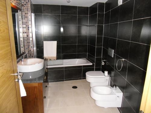 a black tiled bathroom with a toilet and a sink at Casas de Campo Podence in Macedo de Cavaleiros