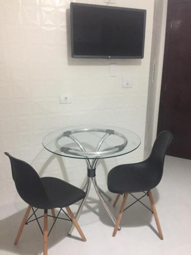 a glass table with two chairs and a tv on a wall at Apartamento pertinho da UEM/Novo Centro in Maringá